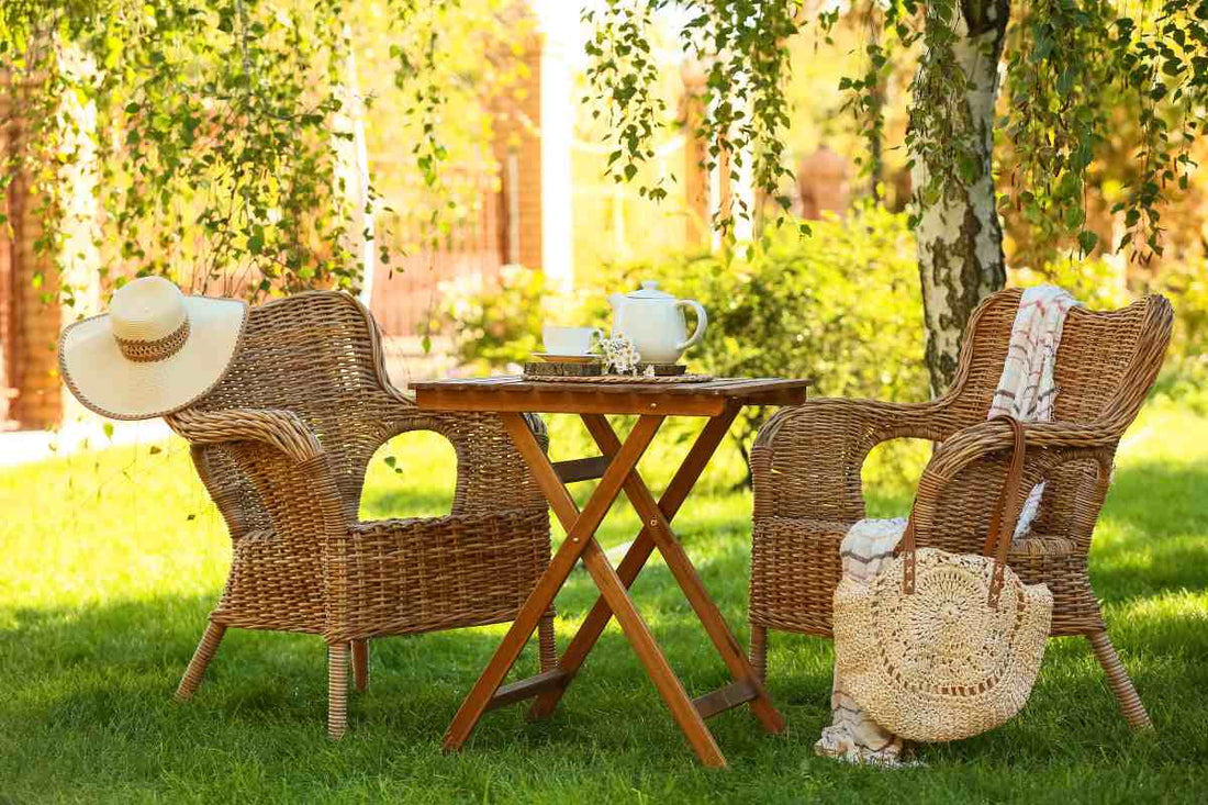 Comfortable wicker armchairs with stylish hat, chamomile flowers and teapot on coffee table in garden