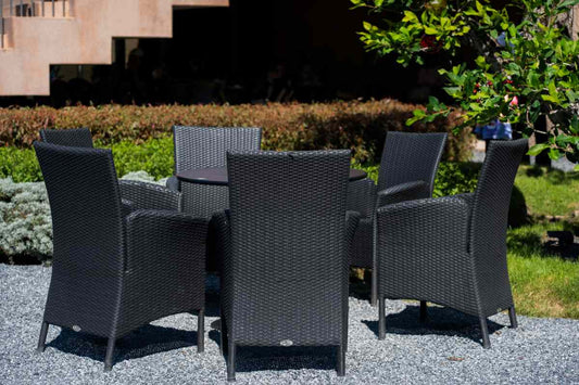 Outdoor dining or seating area with six black synthetic rattan chairs and a matching table in the center, illuminated by sunlight.