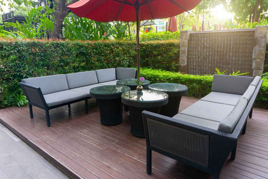 Outdoor rattan furniture with white cushions in the middle of a garden.