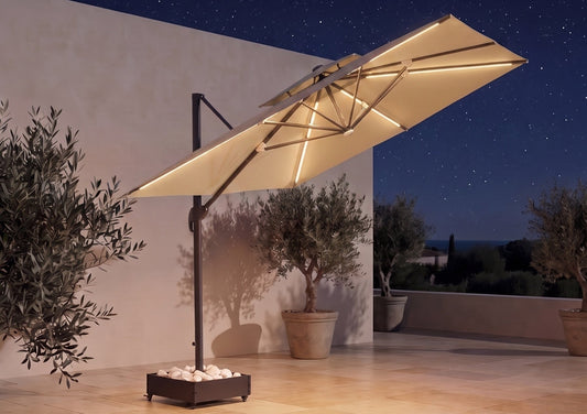 A large cantilevered patio umbrella with a warm cream-colored canopy and integrated warm white LED strip lighting, shown on a stone-tiled outdoor terrace at night under a starry sky.